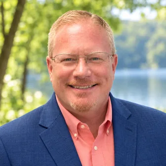 Headshot of Kevin G. Bays, M.D., smiling outdoors in rimless glasses, a navy blazer and a coral shirt.