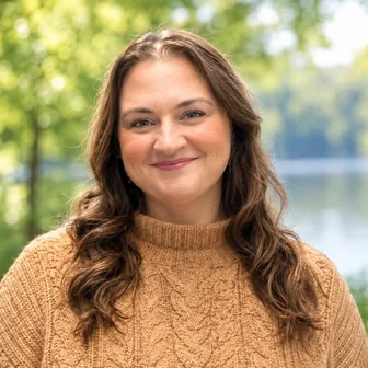 Headshot of Sarah Goff, PMHNP, smiling outdoors with long wavy brown hair and a tan cable-knit sweater.